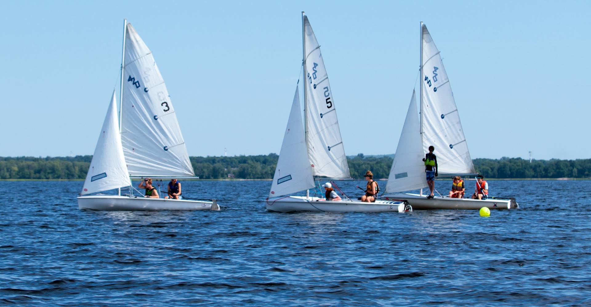 Three 420 training boats crewed by children sail in a row