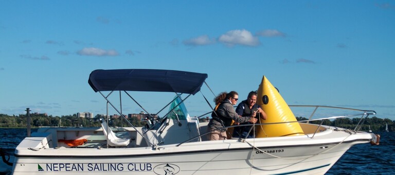 Two race committee volunteers prepare to set a large yellow race marker from the motorboat