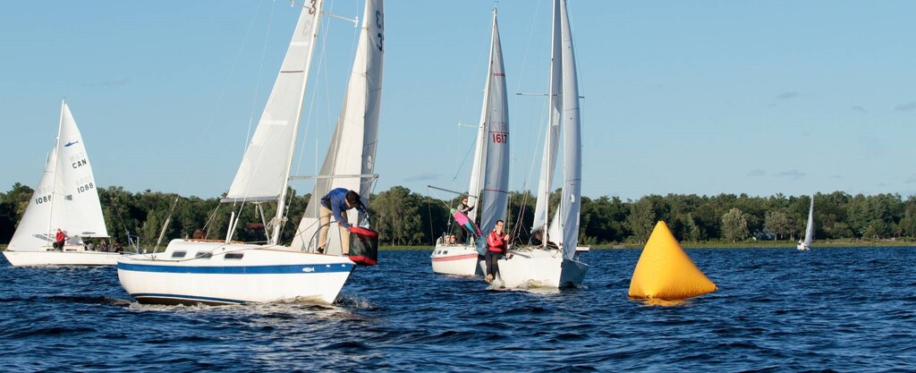 Three sailboats race to turn at a yellow buoy mark