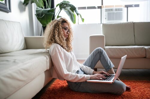 Woman with laptop sitting on floor at home leaning on sofa 