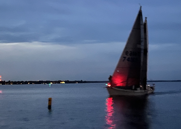 A sailboat racing at night with a light on the bow.