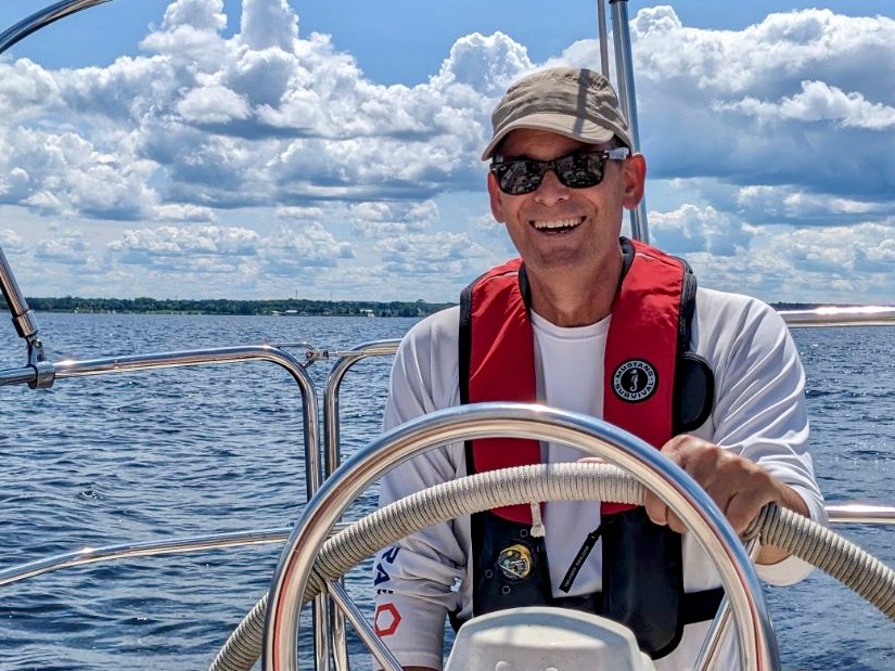 Jim Love at the steering wheel of a sailboat. 